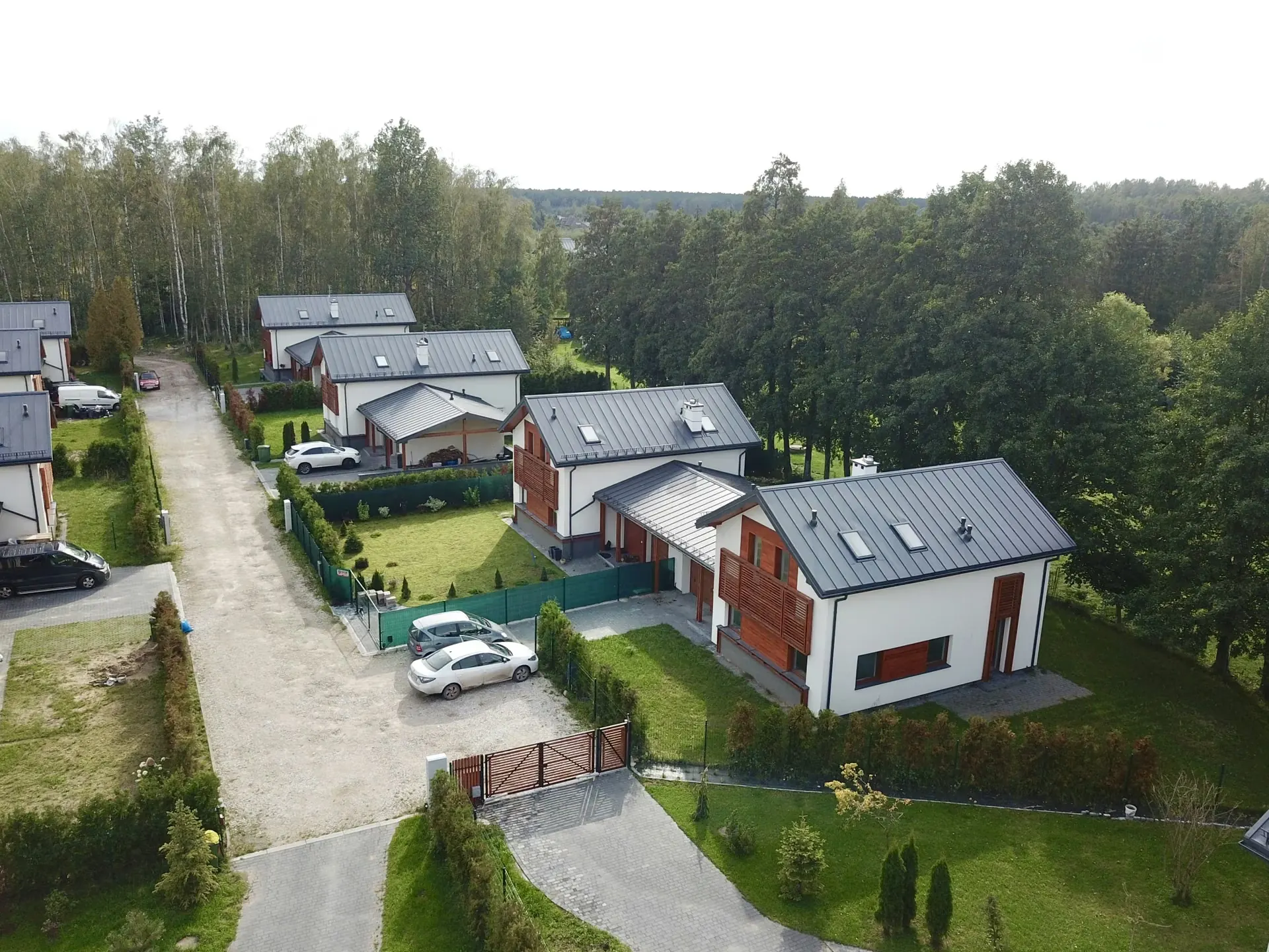 Drone shot osiedla domów jednorodzinnych z drewnianymi akcentami elewacyjnymi, podjazdami i ogrodami w okresie letnim