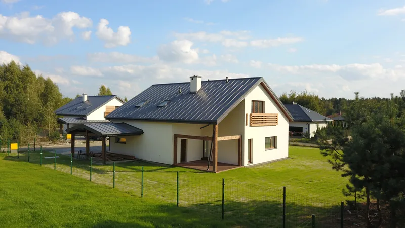 Lotnicze zdjęcie tradycyjnego domu z dwuspadowym dachem i drewnianymi akcentami, otoczonego zielonym ogrodem