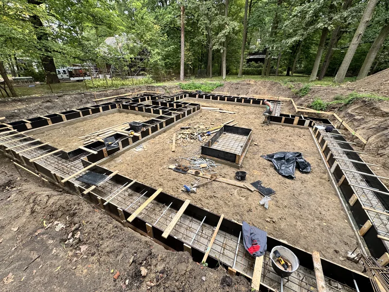 Wykop fundamentowy z gotową siatką zbrojeniową i szalunkami w jesiennym lesie, narzędzia i robotnik w tle